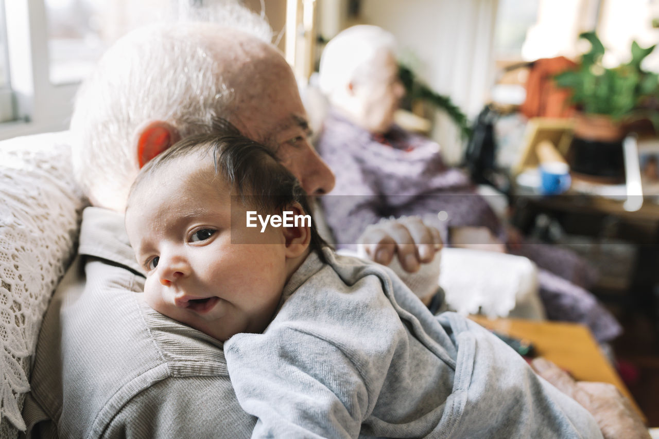 Great-grandfather holding baby at home with his wife in background