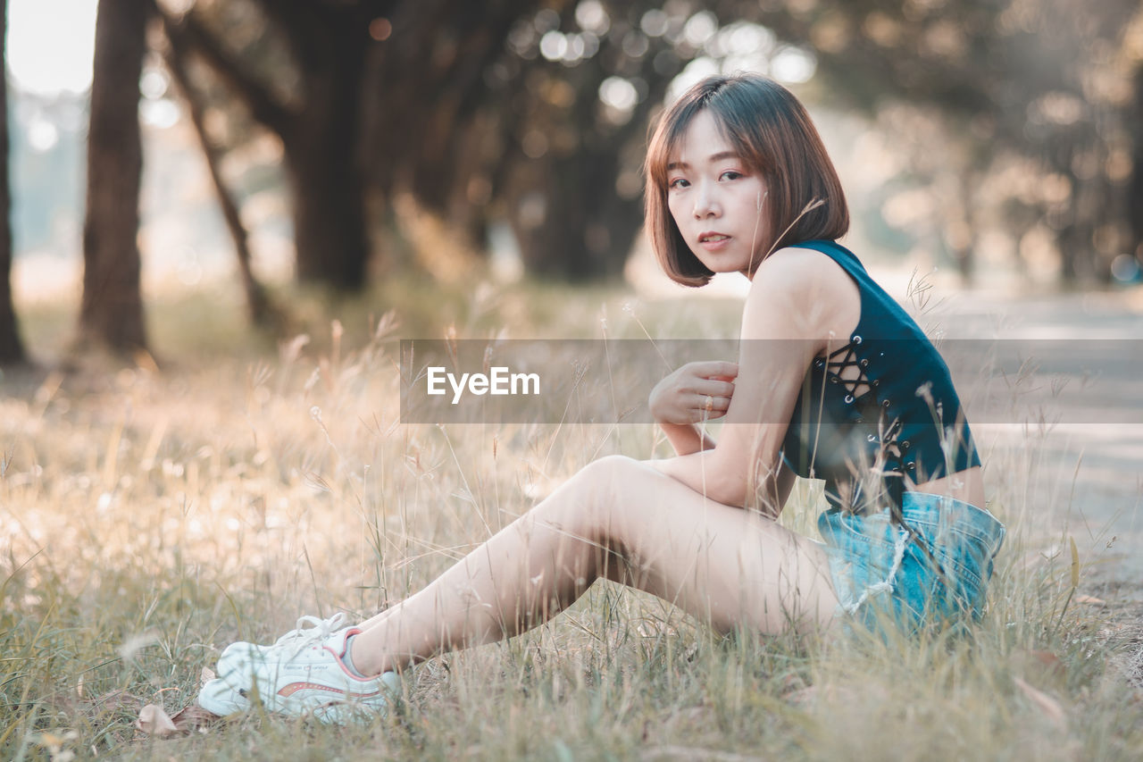 SIDE VIEW OF WOMAN SITTING ON FIELD DURING RAINY DAY