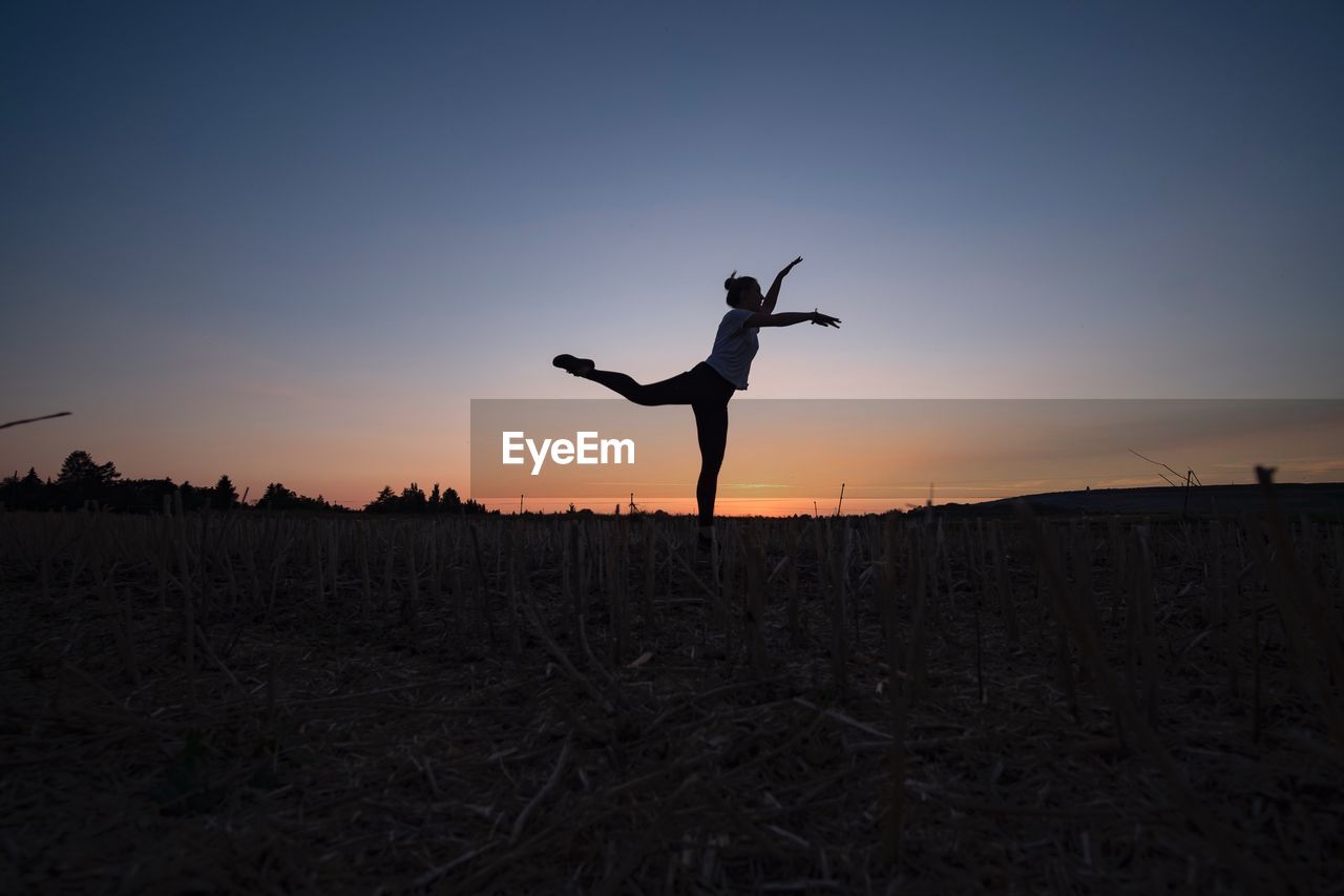 Silhouette young woman exercising on field against sky during sunset