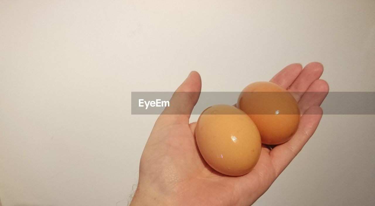 Cropped image of hand holding eggs against beige wall