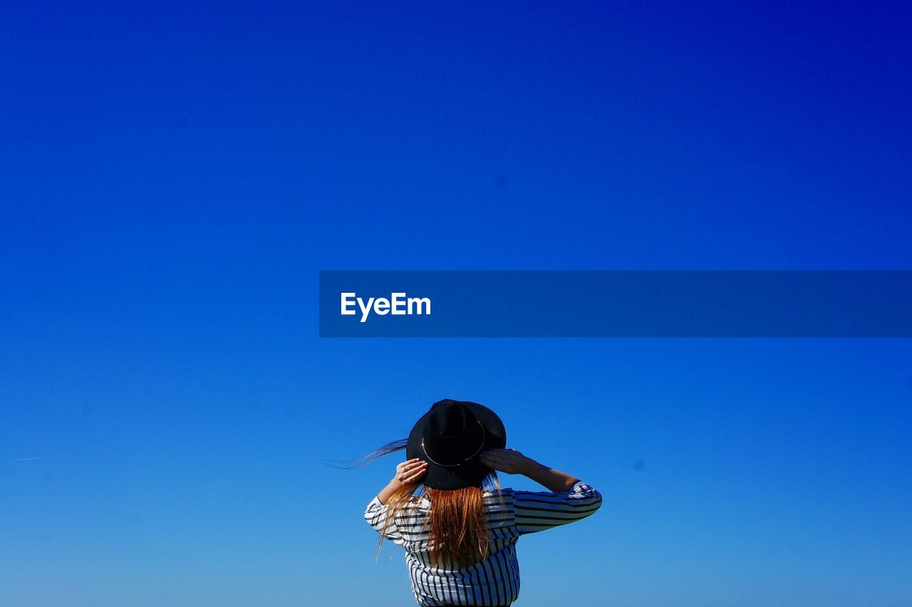 Rear view of woman wearing hat standing against clear blue sky during sunny day