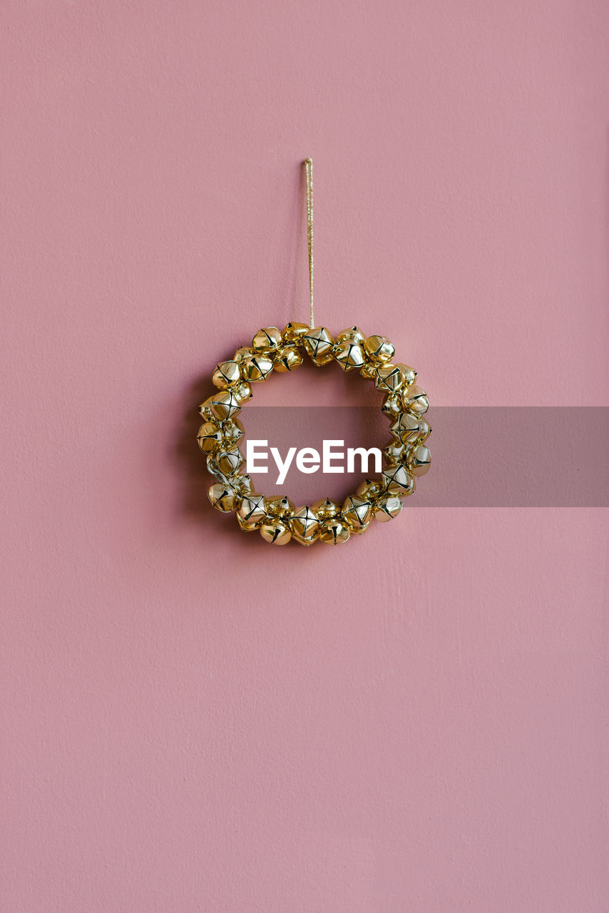 Stylish christmas wreath of golden bells on a pink background with copyi space