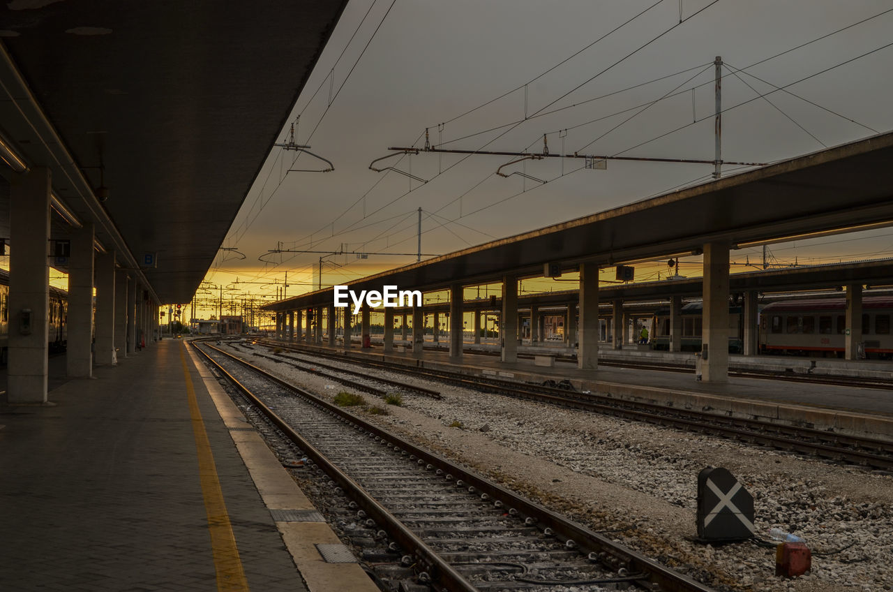 TRAIN ON RAILROAD STATION PLATFORM AGAINST SKY AT DUSK