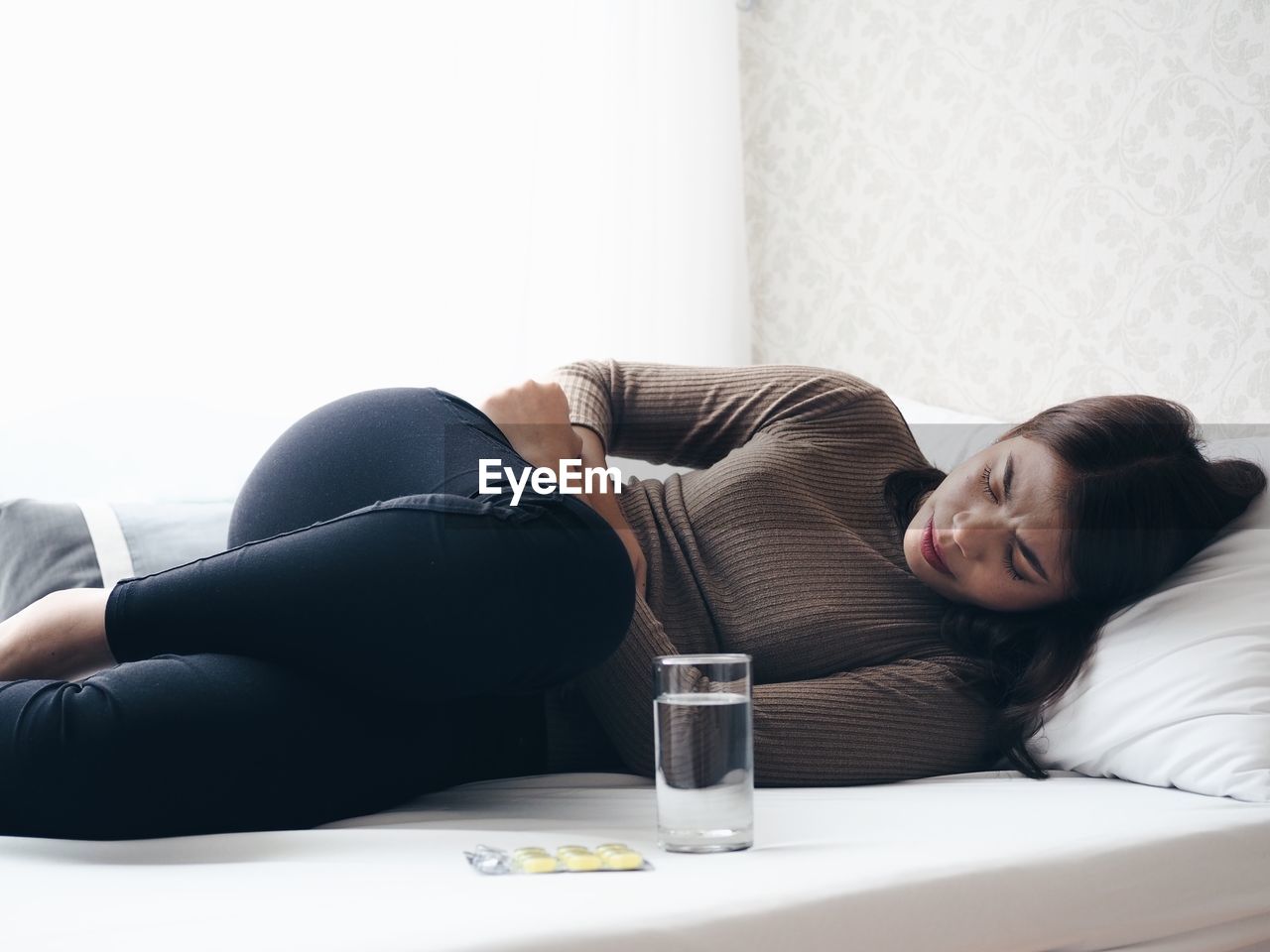 Woman with stomachache lying down on bed at home