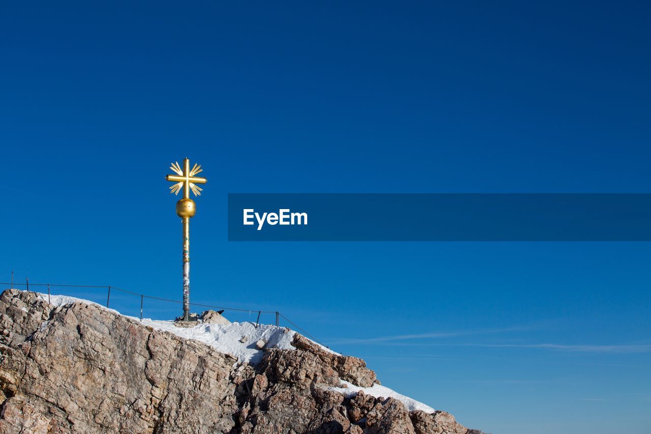 Low angle view of gold cross on mountain against clear blue sky on sunny day