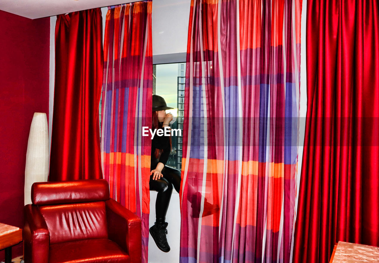 curtain, interior design, one person, adult, indoors, stage, red, room, furniture, full length, chair, window treatment, young adult, standing, business, men, window covering, clothing, arts culture and entertainment, occupation, lifestyles