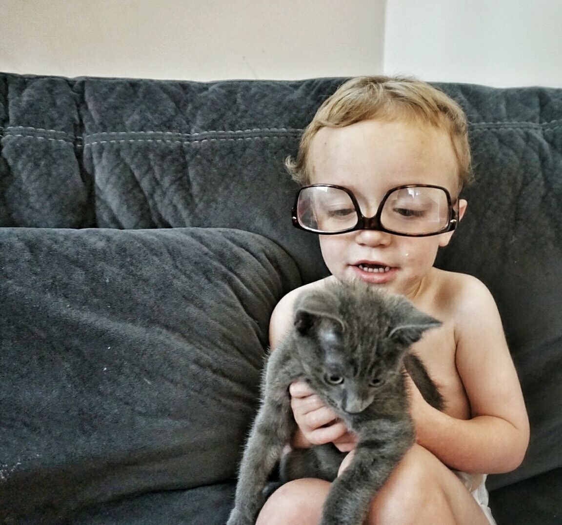 Boy holding cat while sitting on sofa at home