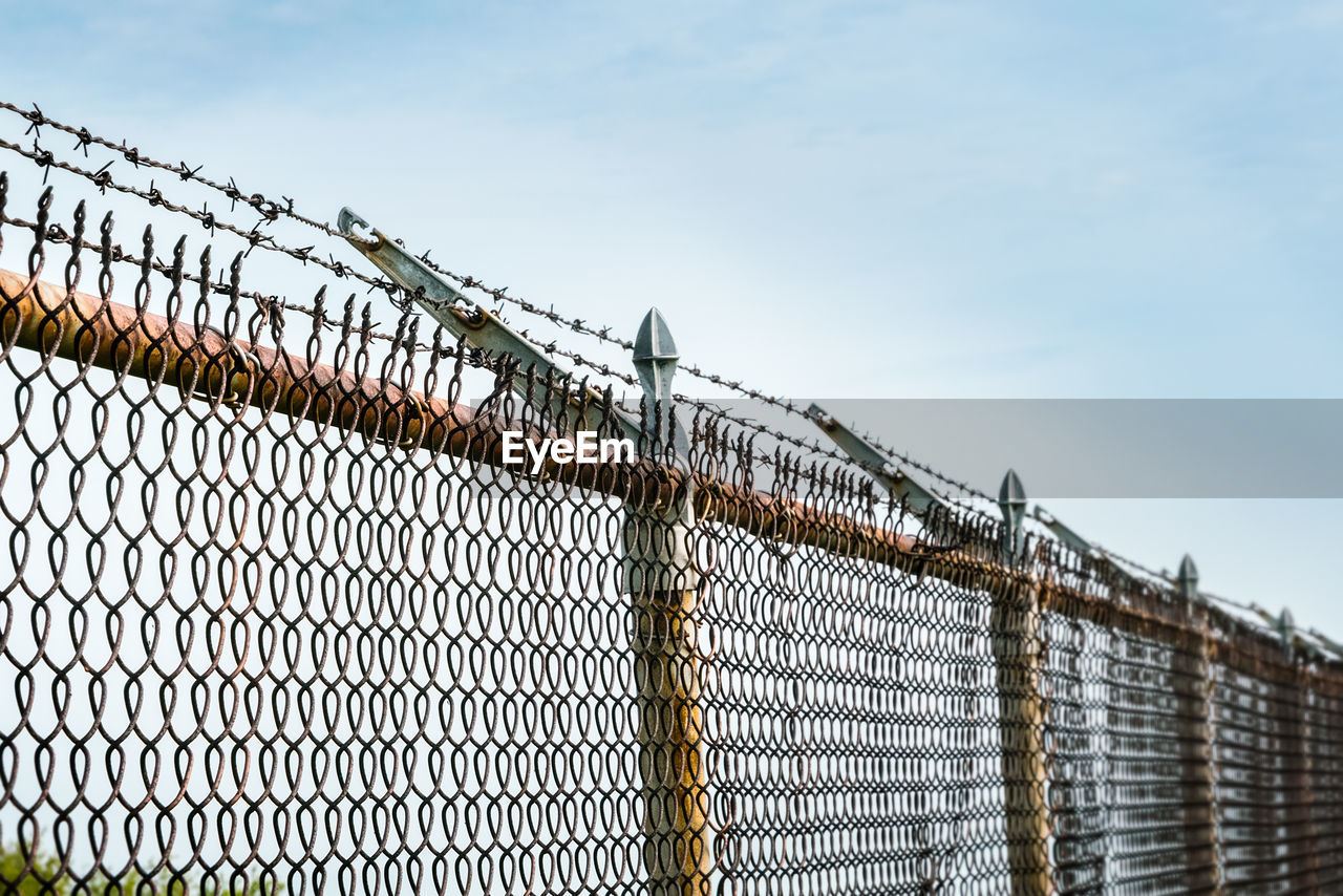 A long length of chain link fence topped with barbed wire set against cloudy sky - trapped