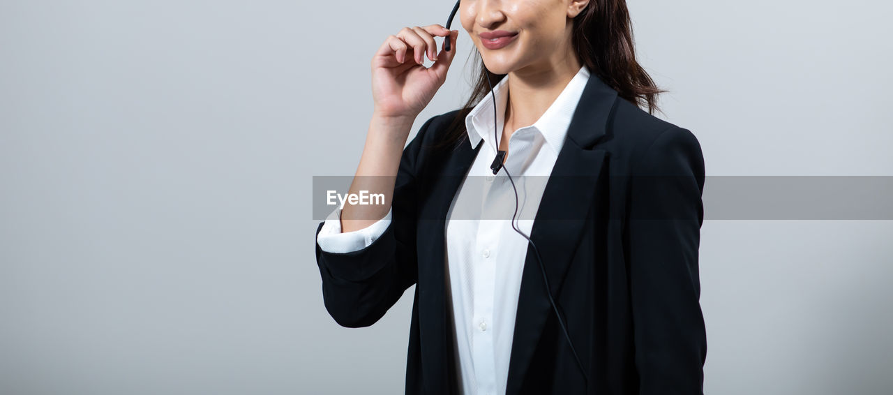 MIDSECTION OF WOMAN WITH MOBILE PHONE AGAINST WHITE BACKGROUND