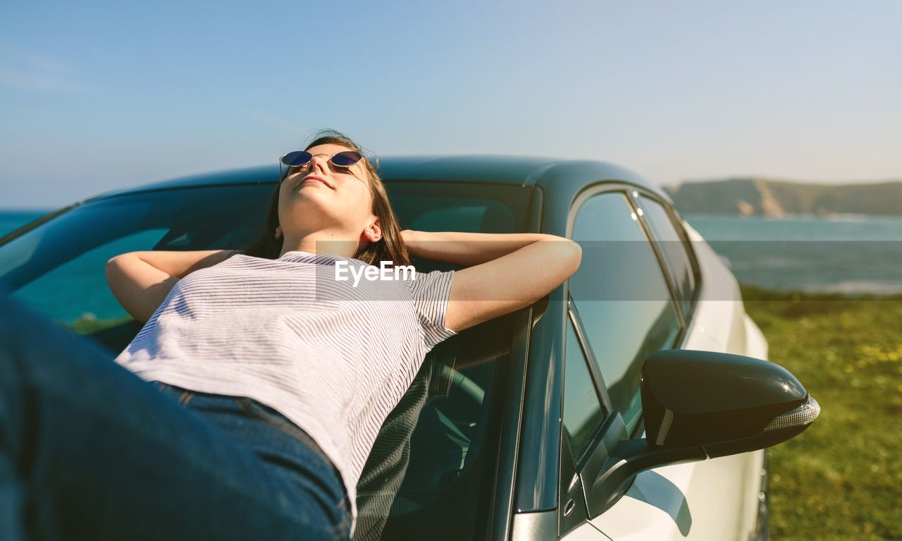 Young woman lying on car at beach