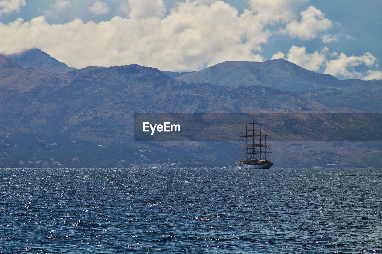 Sailboat sailing on sea by mountains against sky