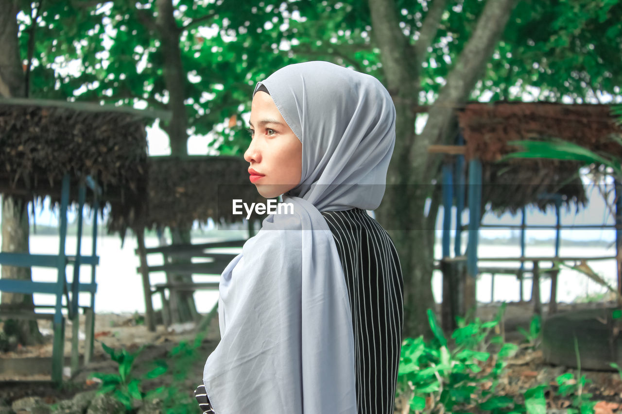 Portrait of beautiful young woman standing against trees