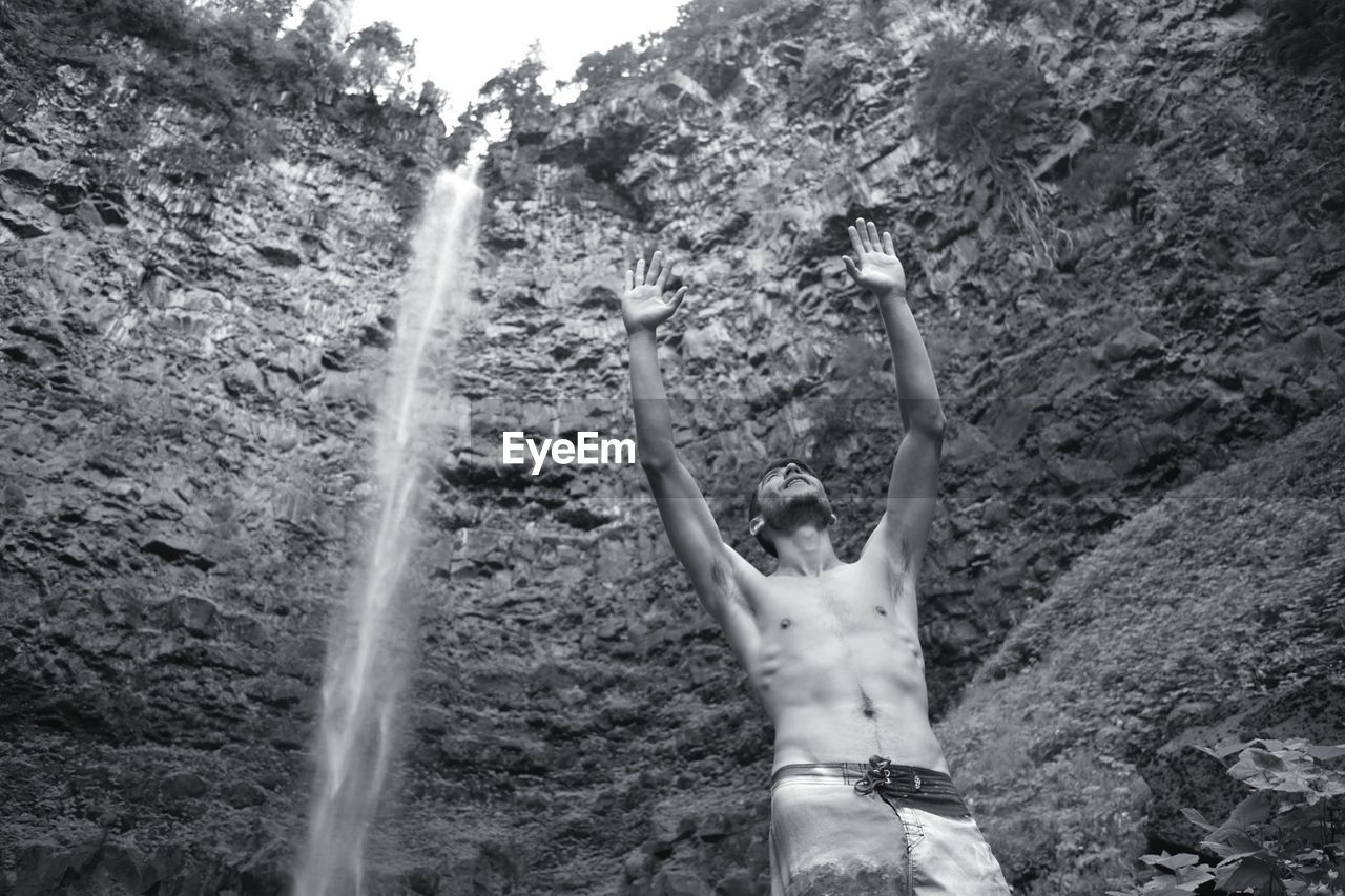 Low angle view of shirtless man standing against waterfall