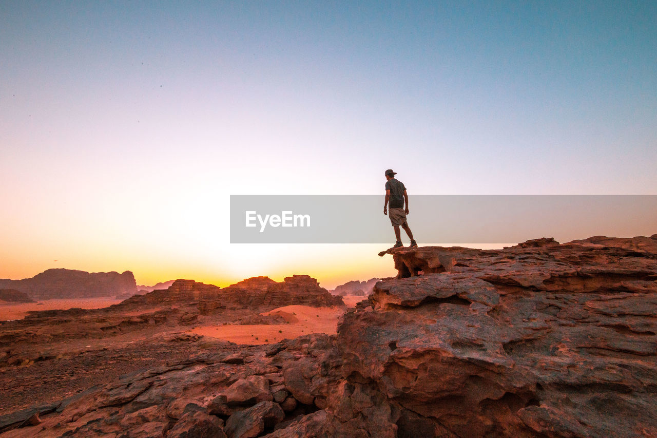 Man standing on rock at wadi rum against clear sky