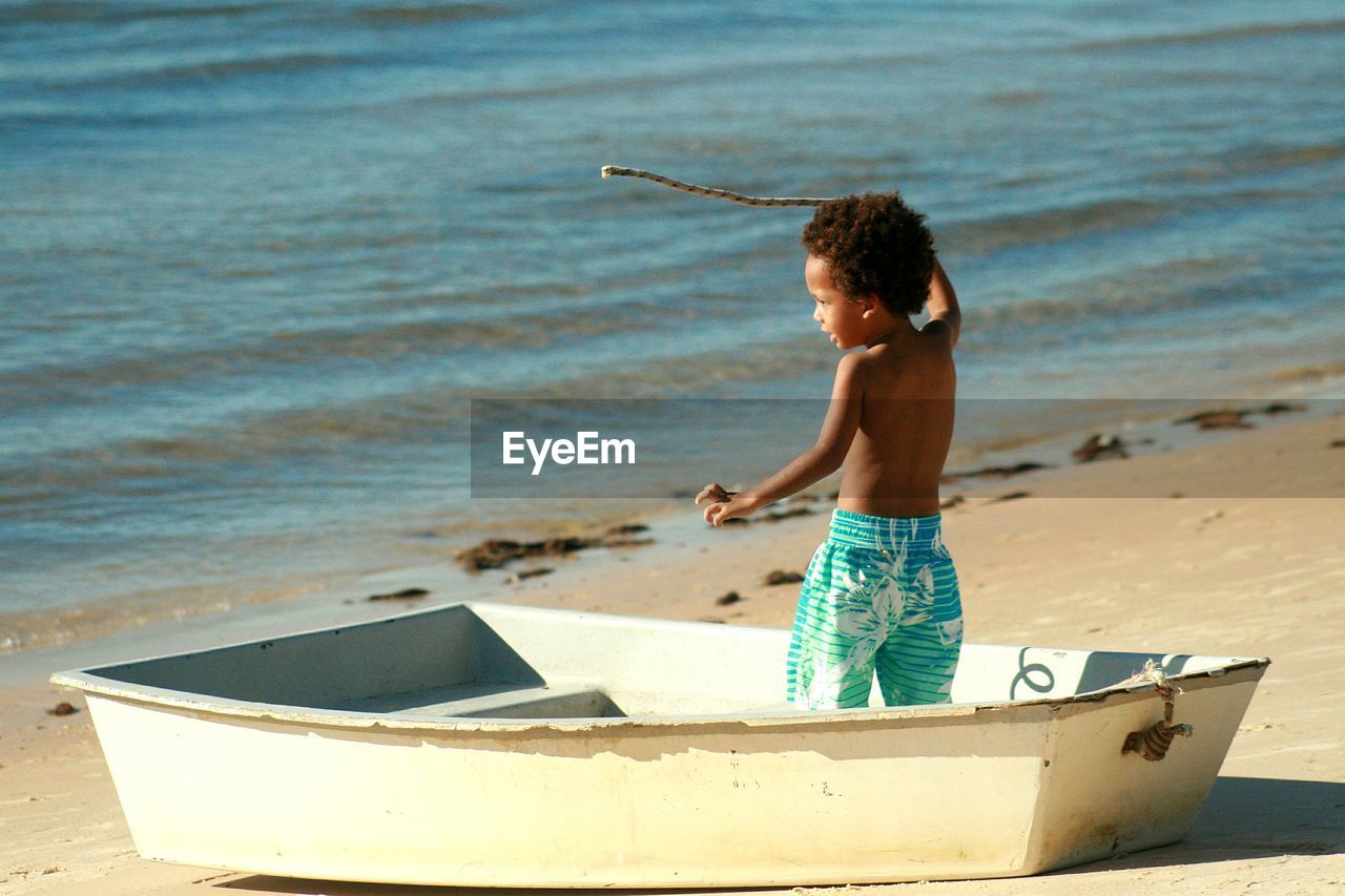 Shirtless boy standing in boat on shore at beach