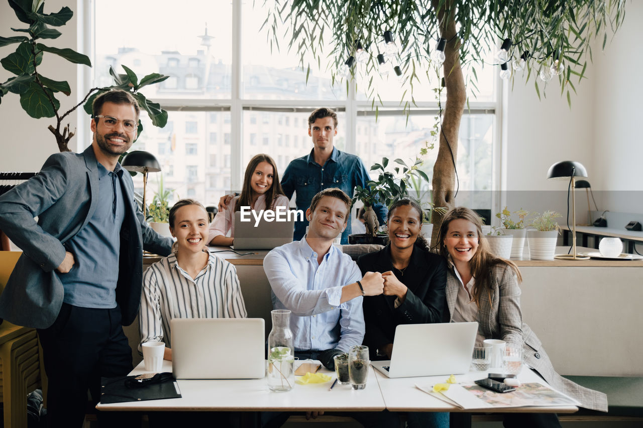 Confident male and female colleagues with laptops at desk in creative office