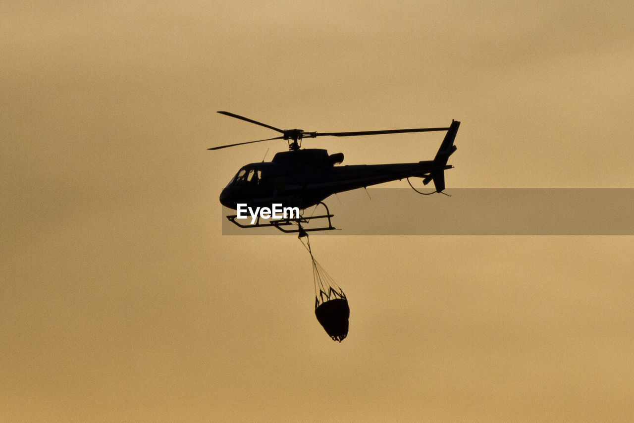 Low angle view of silhouette helicopter with parachute flying against sky during sunset