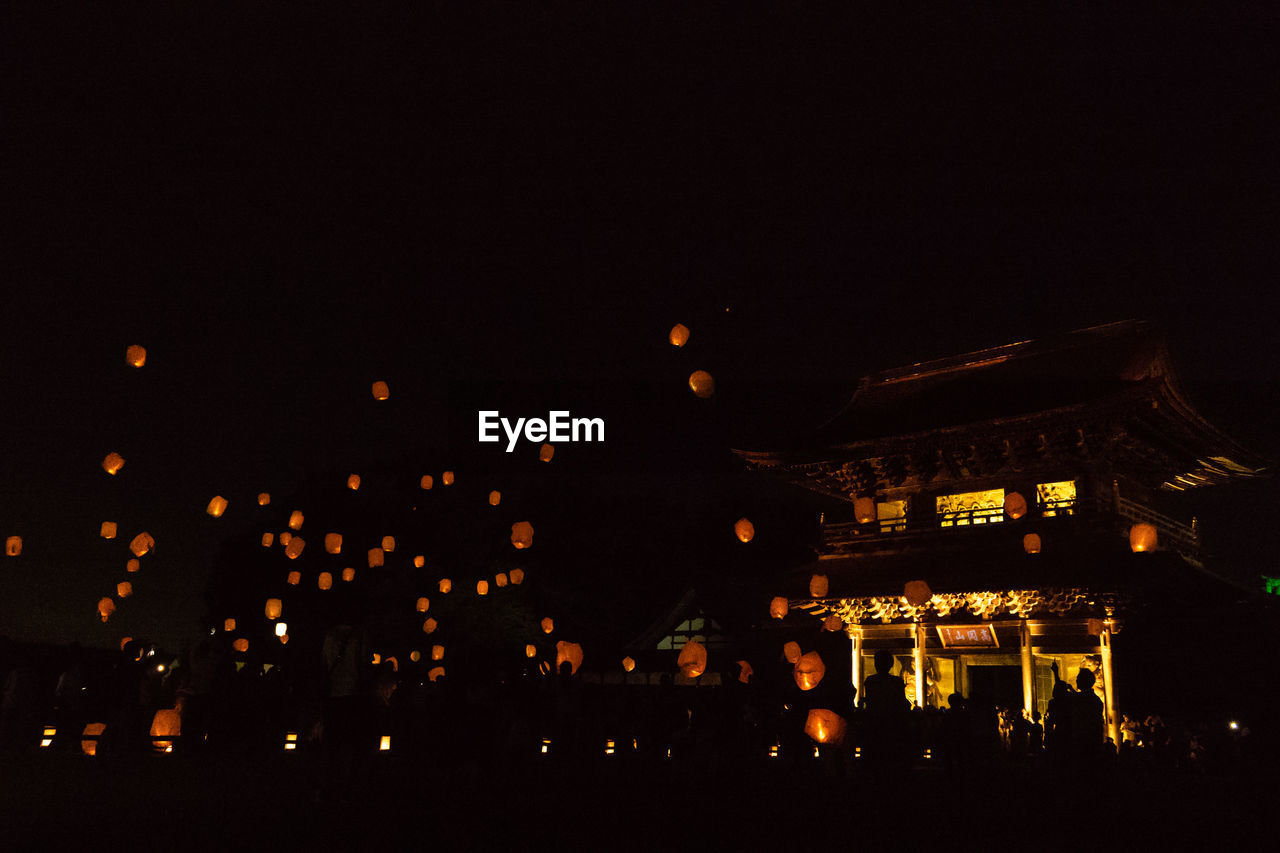 Illuminated paper lanterns flying against sky in city at night