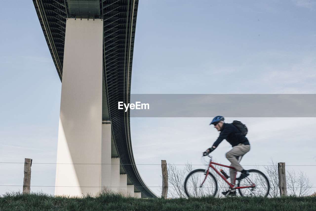 Senior man riding bike, under bridge