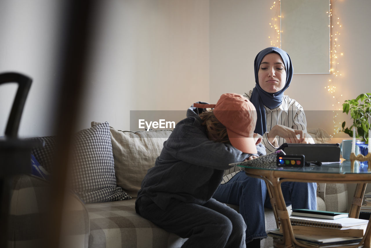 Mother wearing hijab helping tired son with add or adhd doing homework