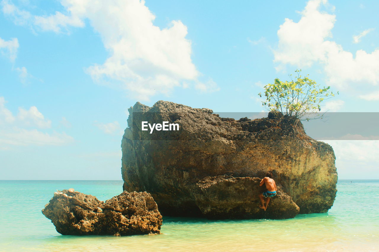 Rear view of man climbing rock in sea