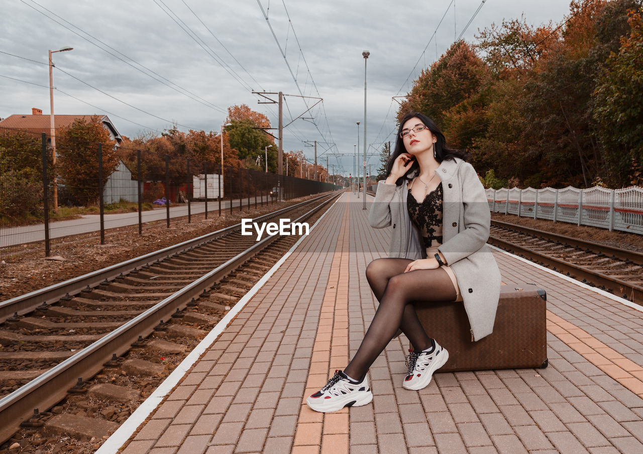 FULL LENGTH OF WOMAN SITTING ON RAILROAD PLATFORM