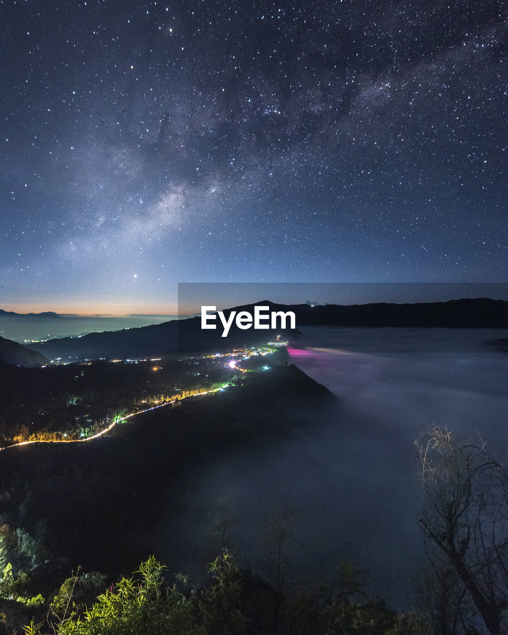 Scenic view of illuminate town by sea against sky at night