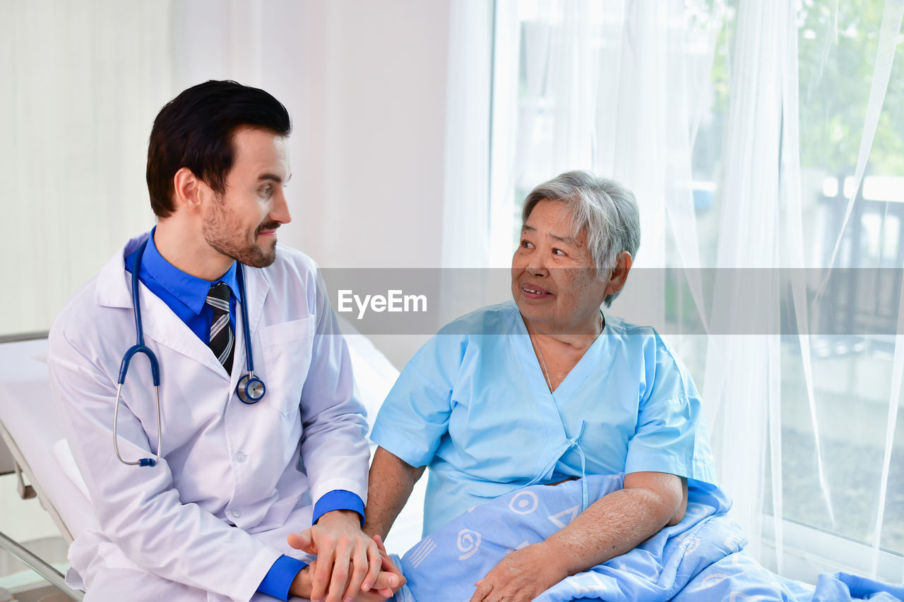 Smiling doctor sitting by senior woman in hospital