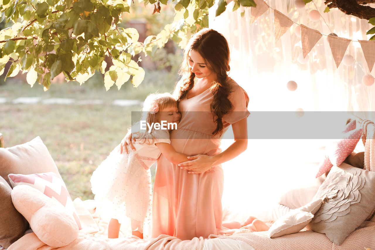 Smiling daughter embracing pregnant mother on bed