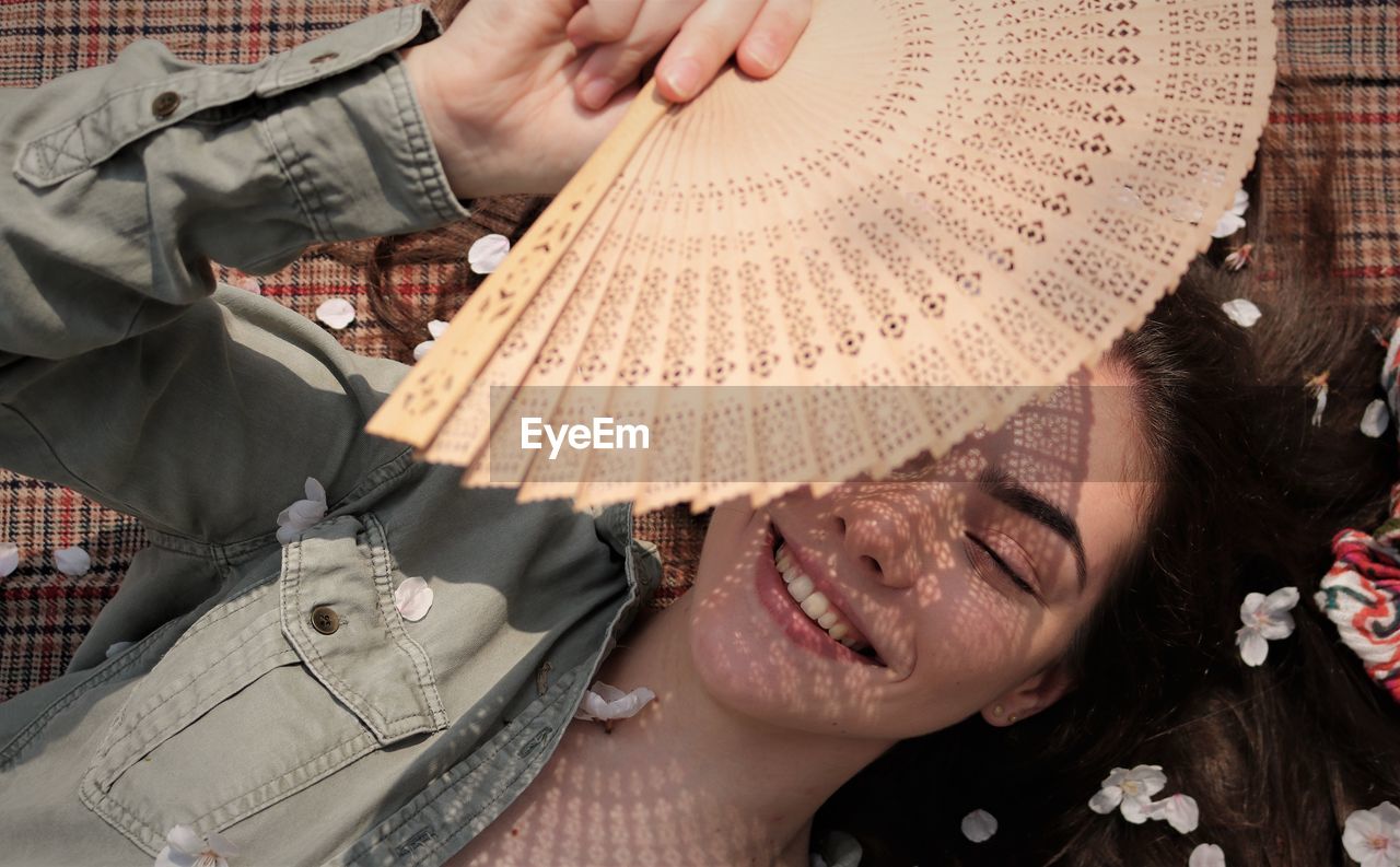 Directly above shot of smiling girl holding hand fan while lying on textile