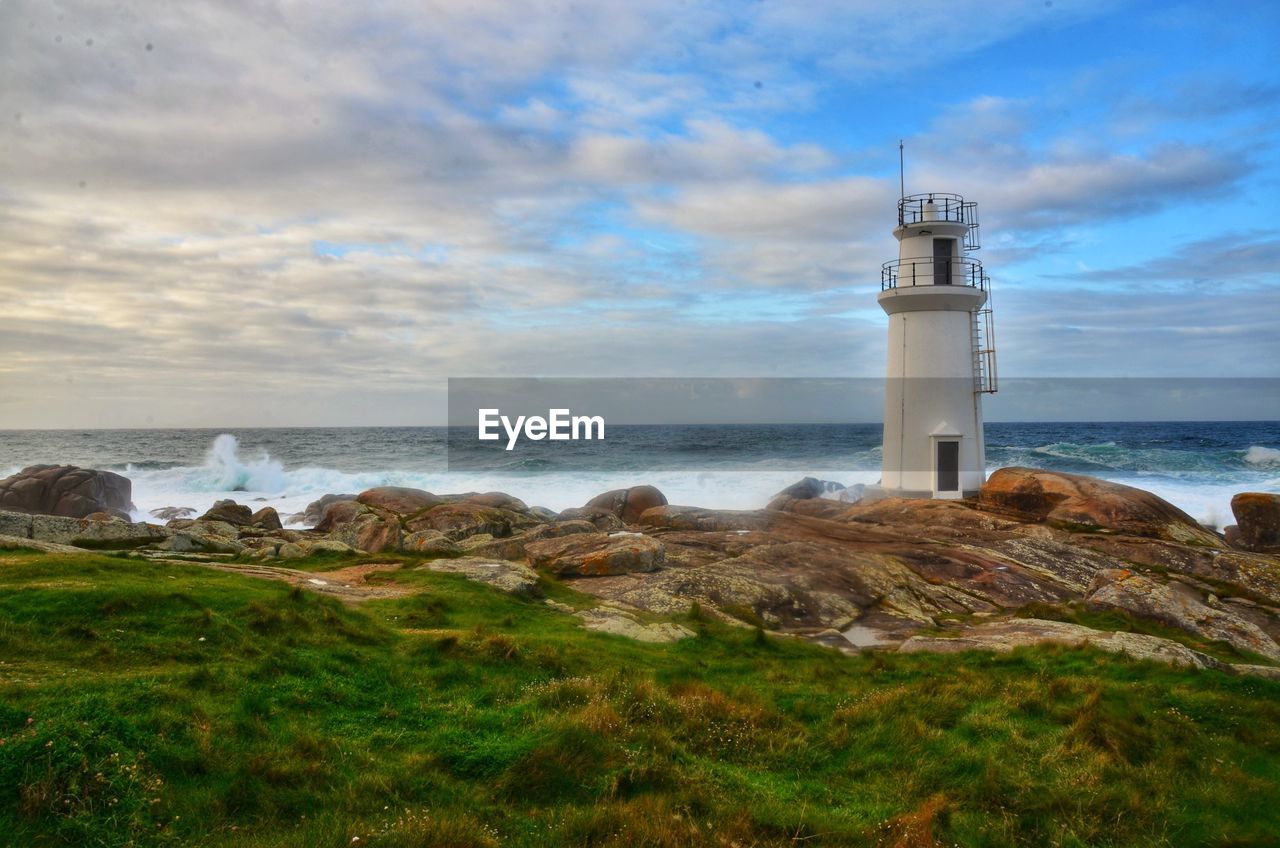 lighthouse by sea against cloudy sky