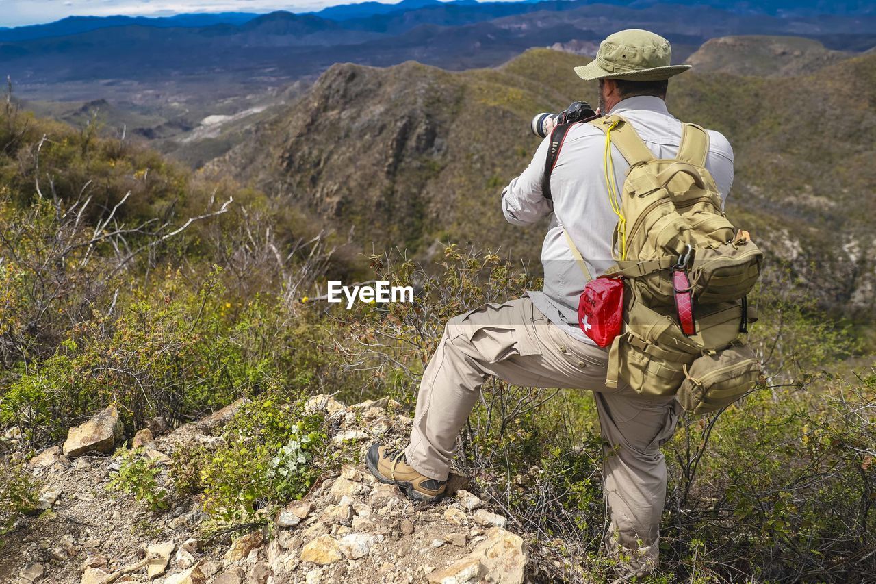 REAR VIEW OF MAN STANDING ON ROCK BY LAND