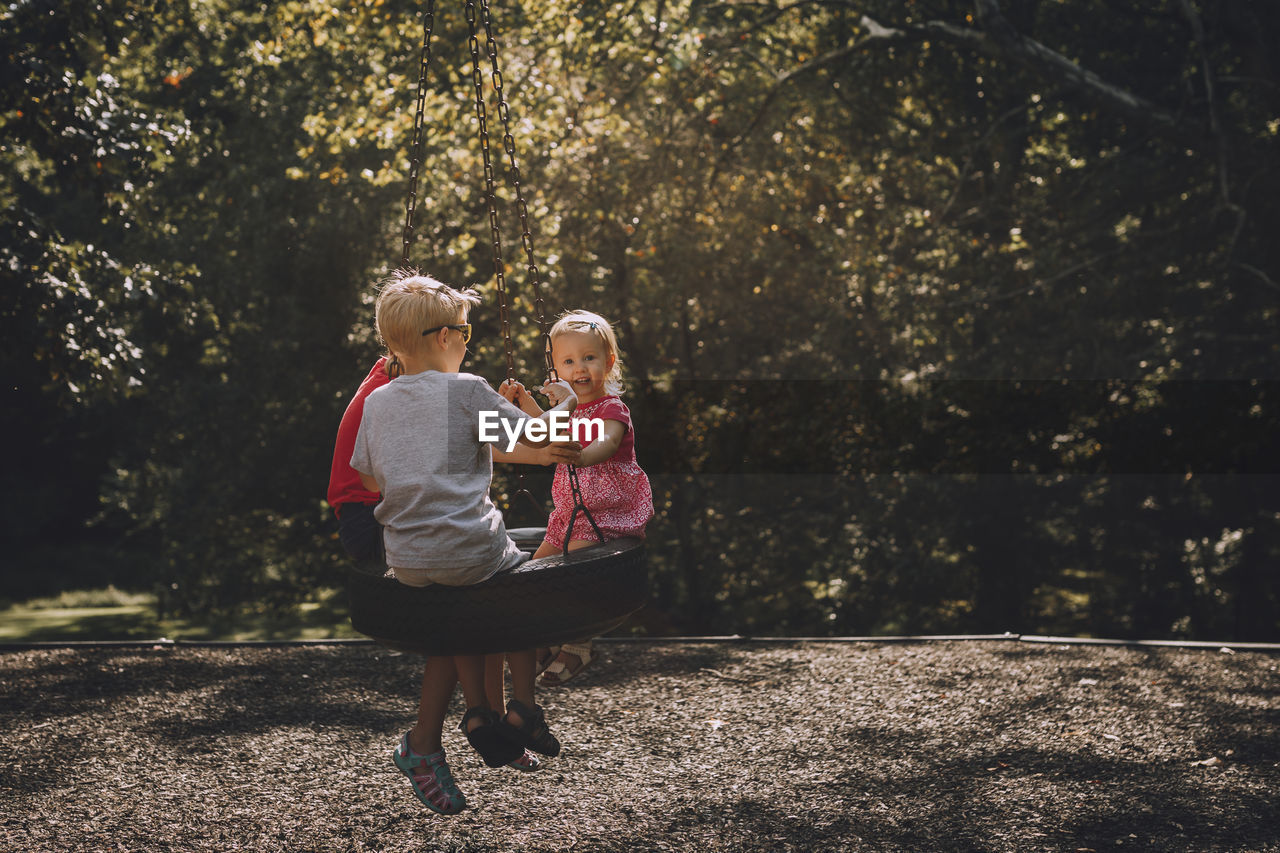 Siblings sitting on swing at park