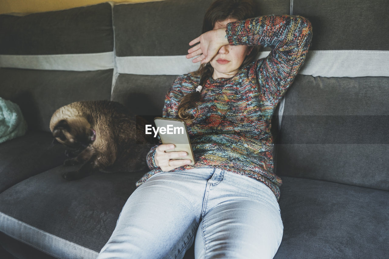 Tired woman with smart phone sitting on sofa