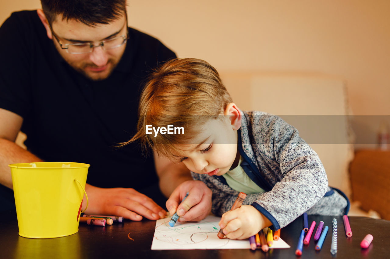 Father and son coloring on table at home