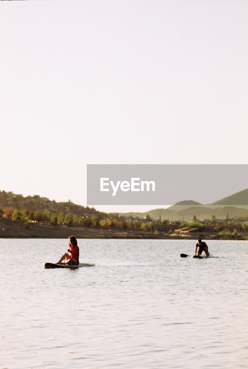 MEN IN BOAT ON LAKE AGAINST CLEAR SKY