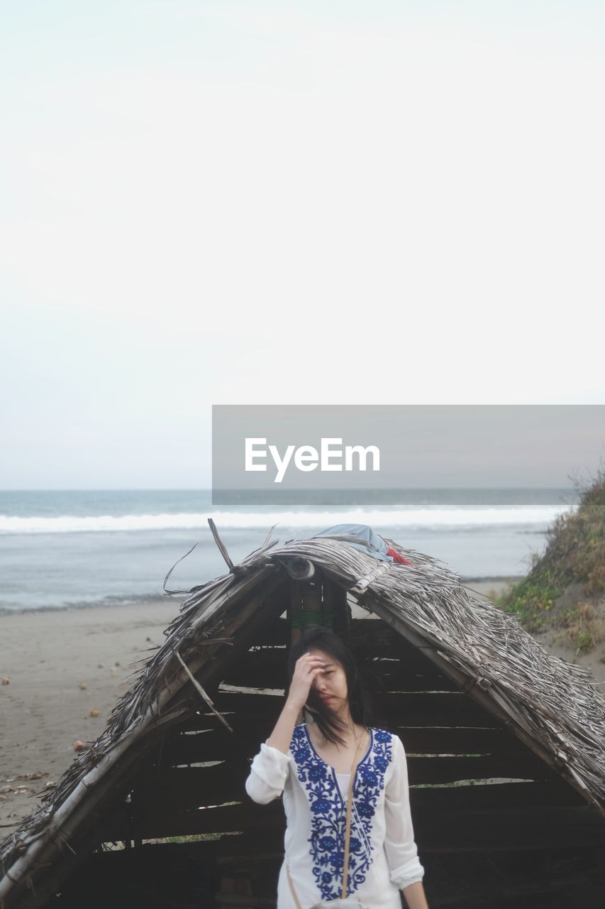 Woman standing by hut at beach against sky