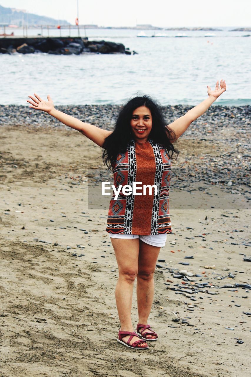 Portrait of happy mature woman with arms outstretched standing at beach