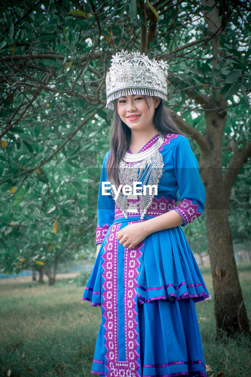 PORTRAIT OF A SMILING GIRL STANDING AGAINST TREES