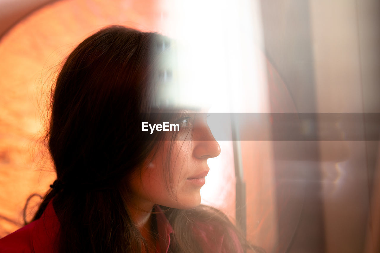 Close-up portrait of young woman looking through window