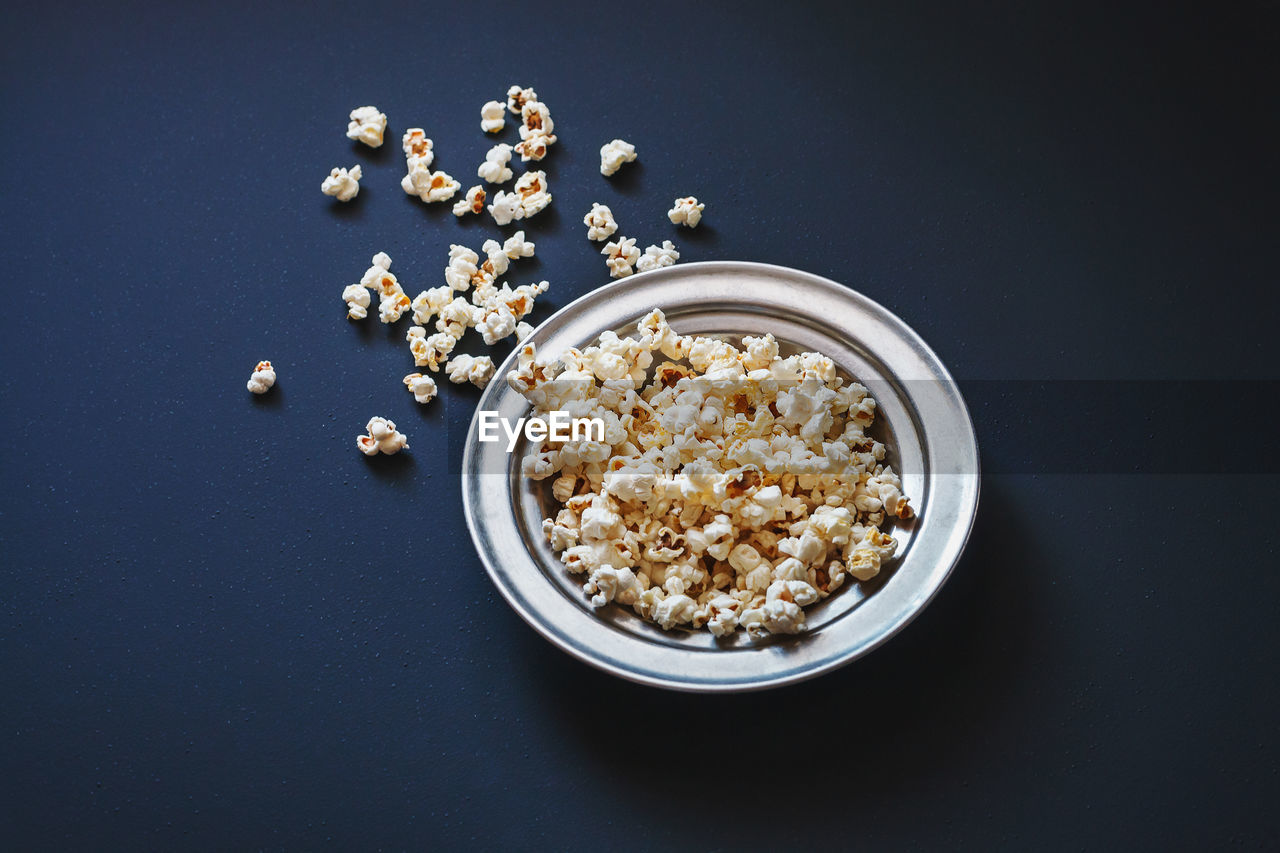 Top view of popcorn in a metallic plate on a matte black surface. tasty source of dietary fiber.