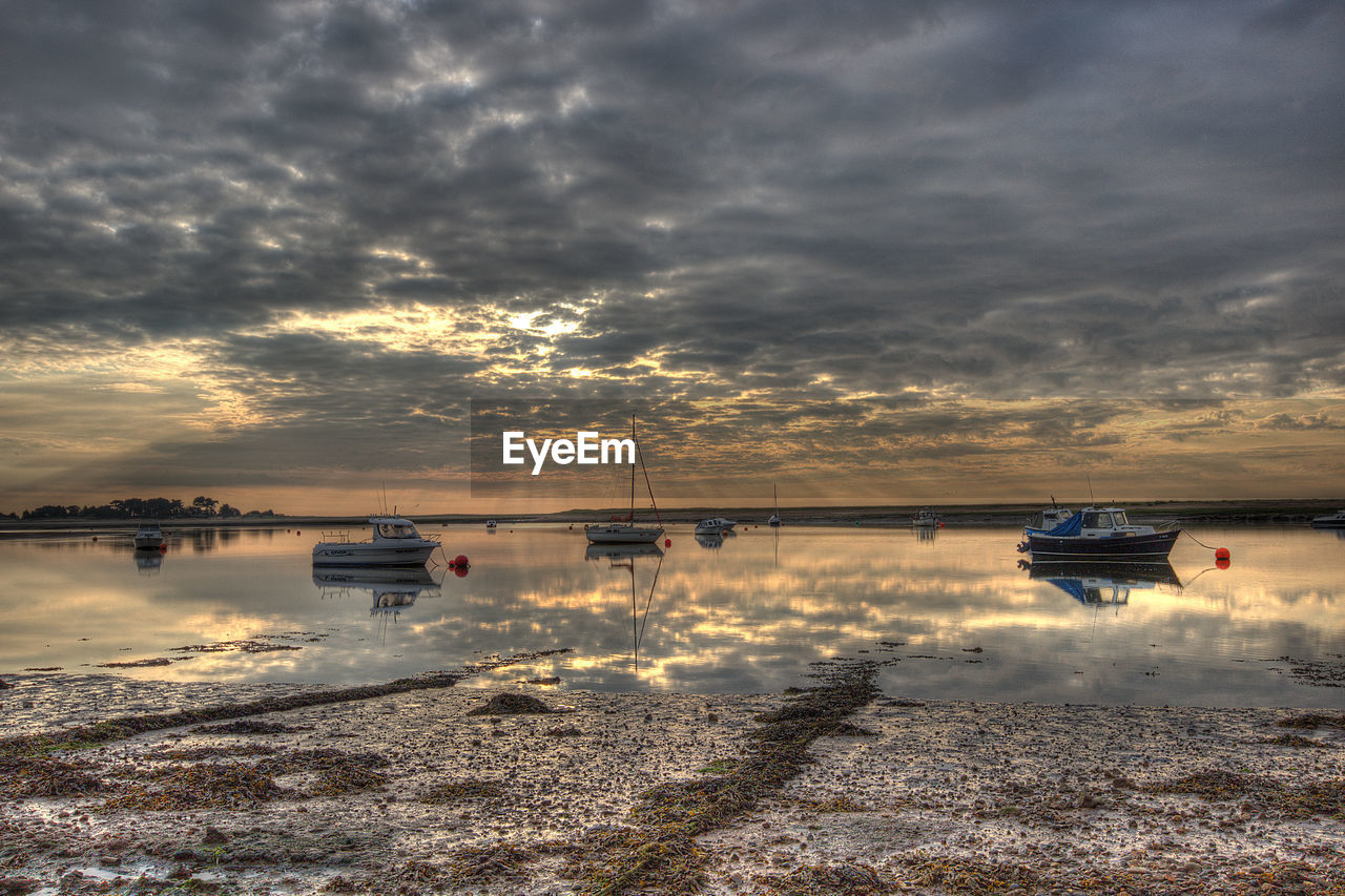 Boats moored on sea against cloudy sky during sunset