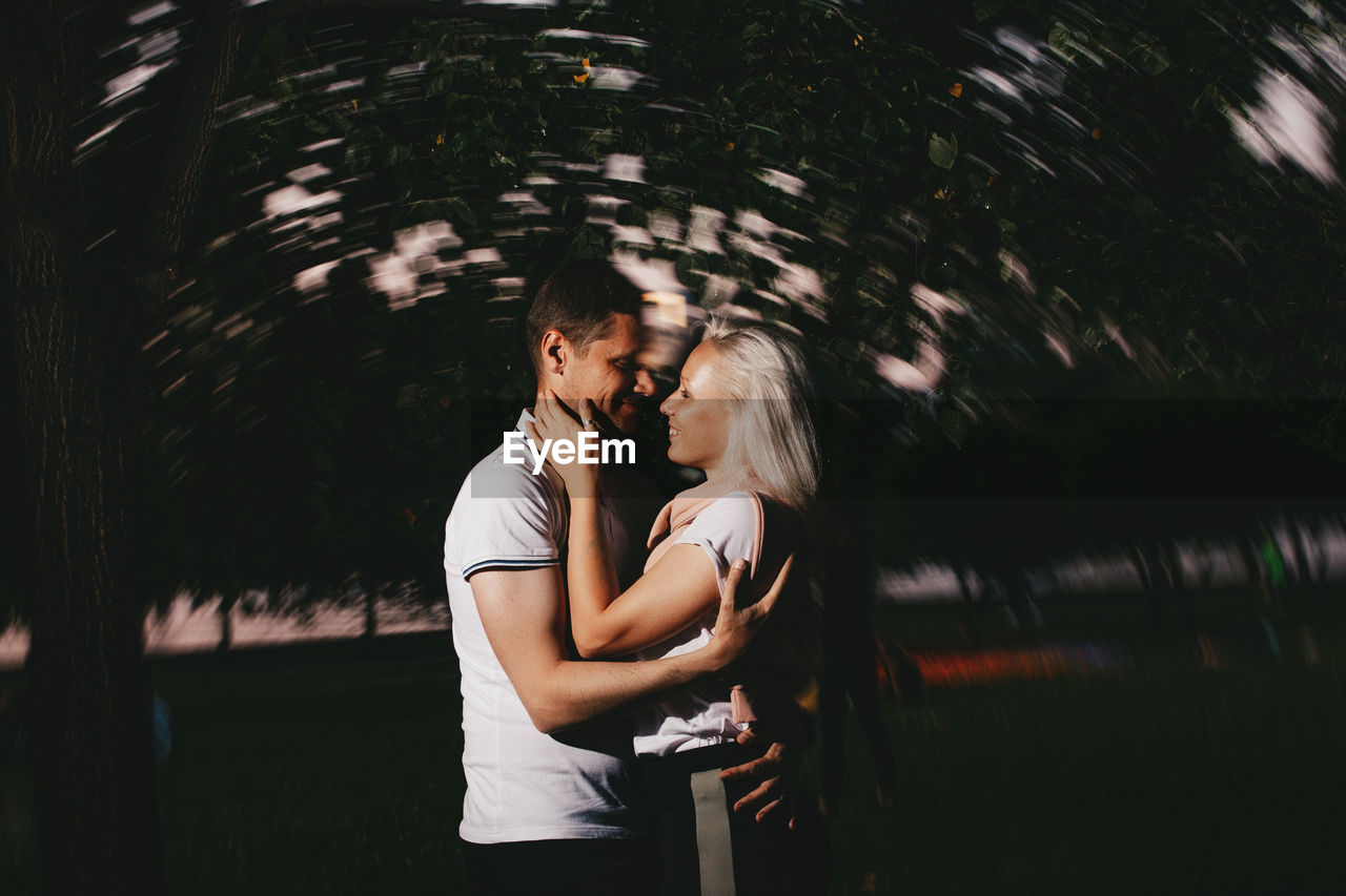 Couple embracing while standing against trees at dusk