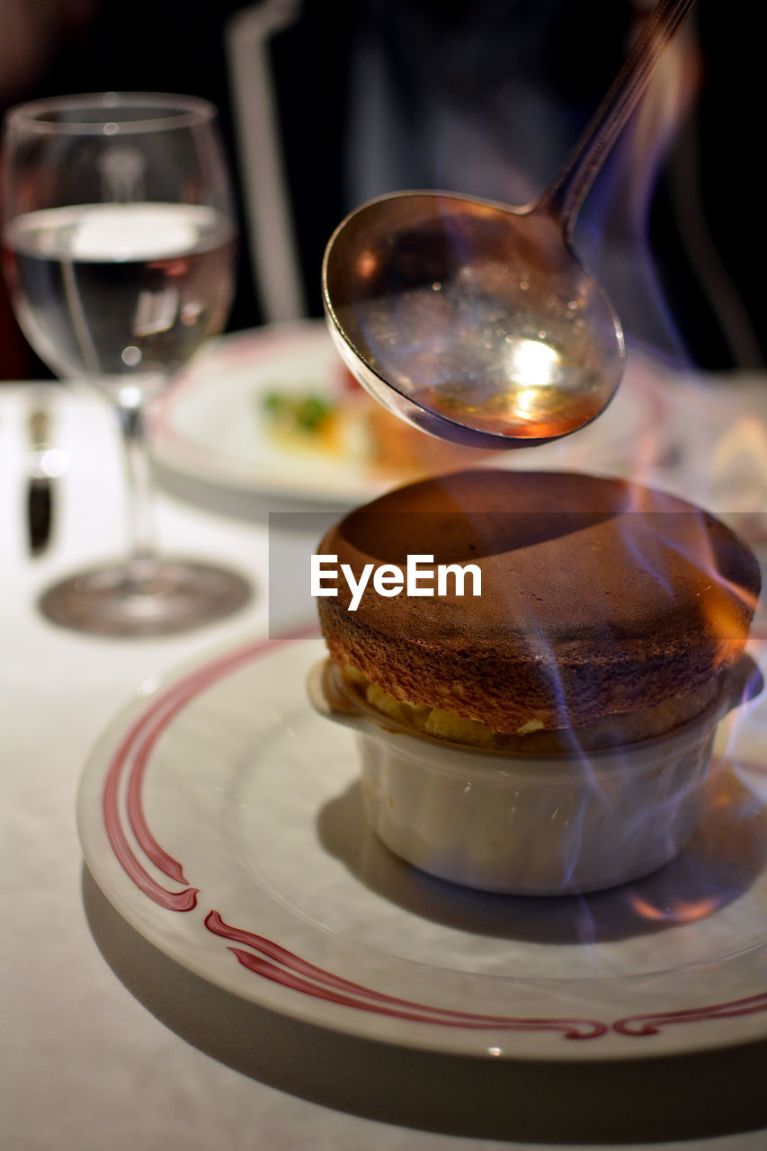 Spoon pouring caramel on flammable dessert souffle served on table