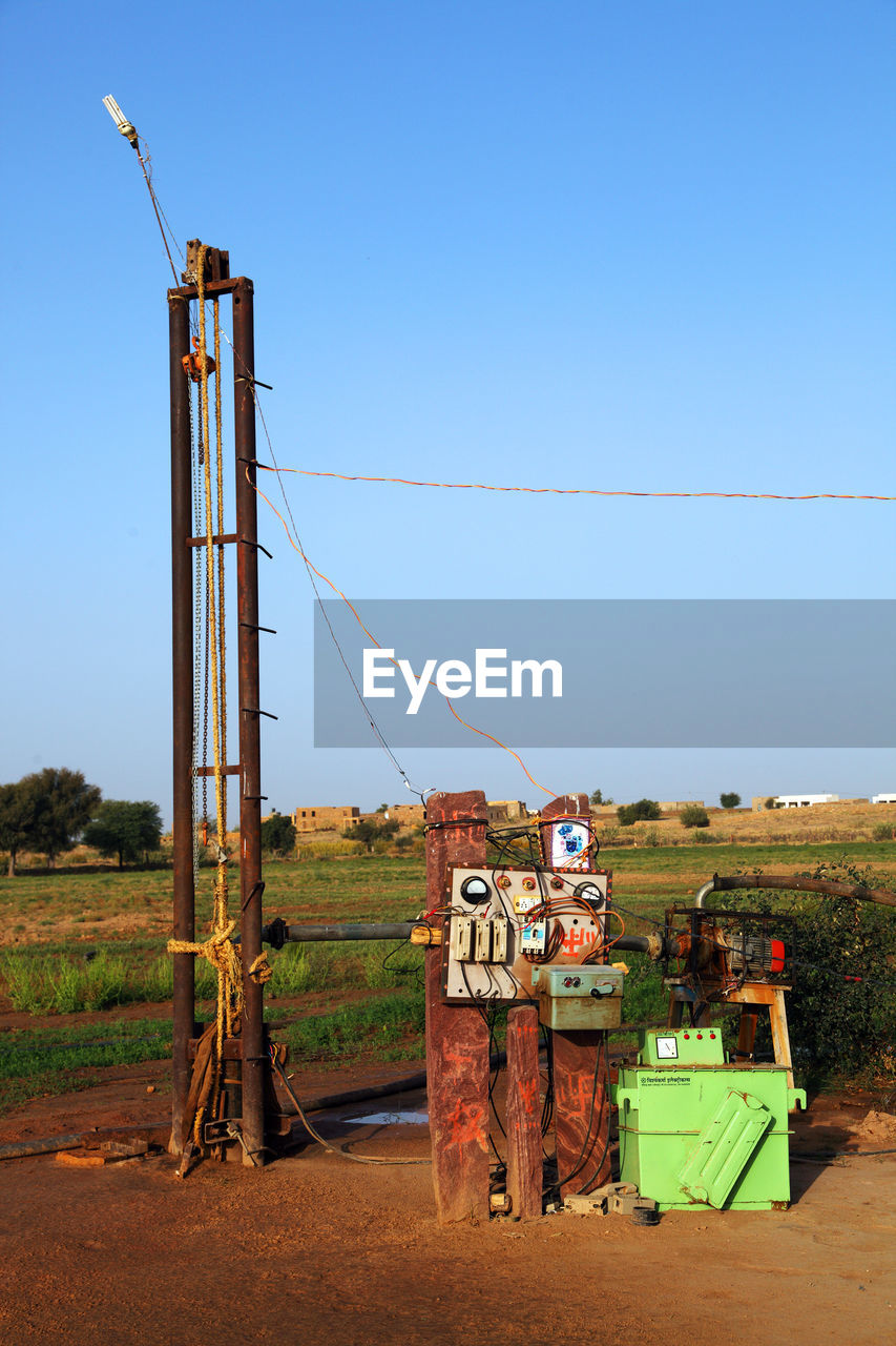 Water drilling machine by grassy field against clear blue sky