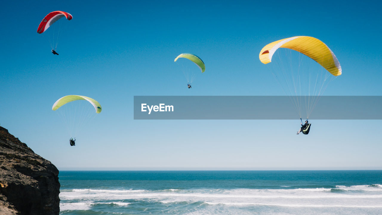 People paragliding at beach against clear blue sky
