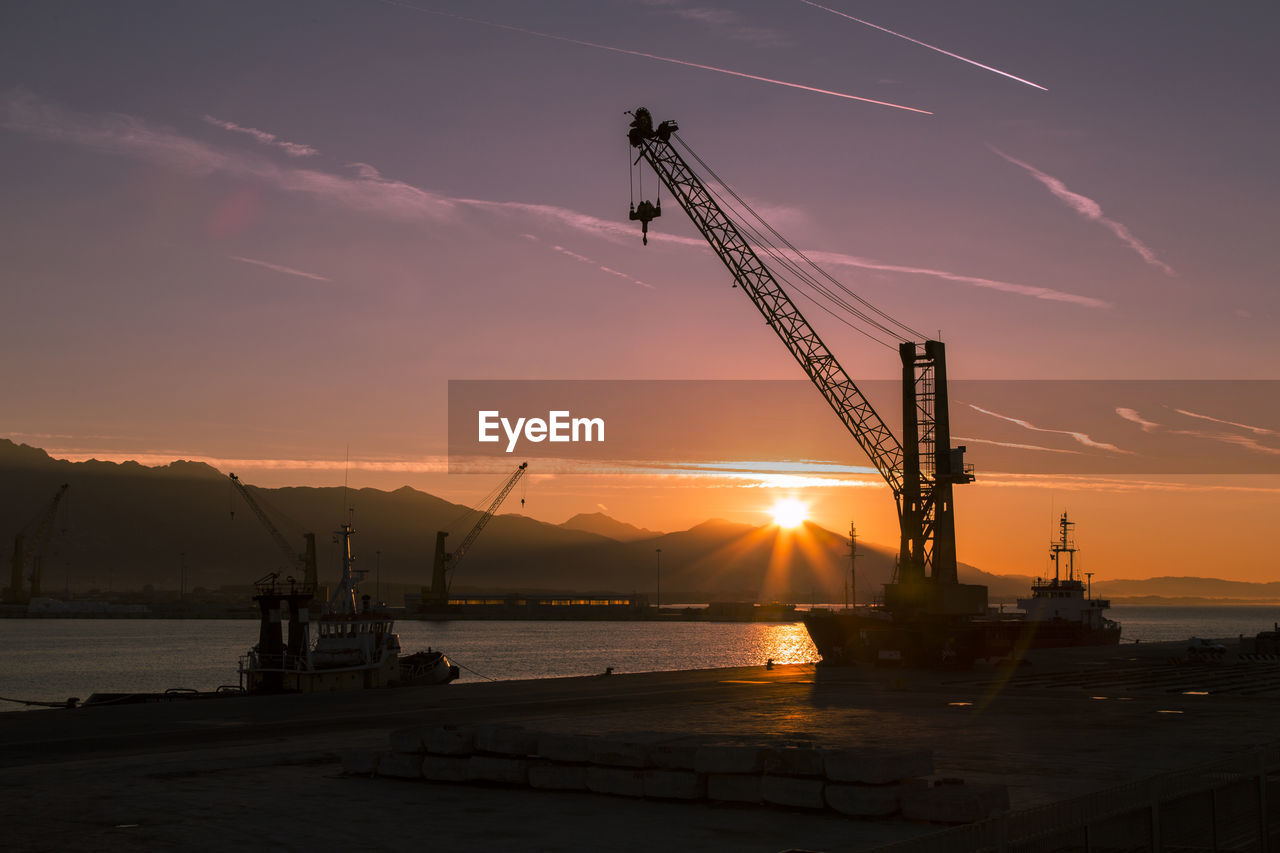 Silhouette crane by sea against sky at sunset