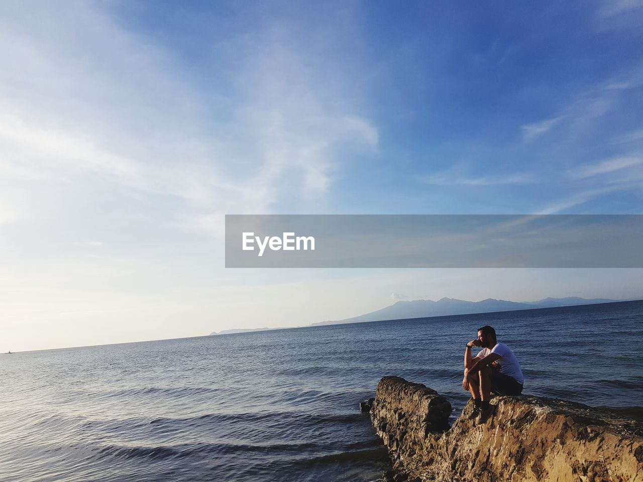 Man sitting on rock looking at sea against sky