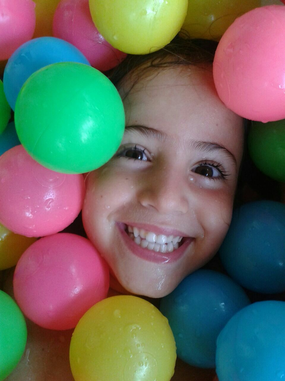 Close-up portrait of smiling wet girl surrounded with multi colored ball