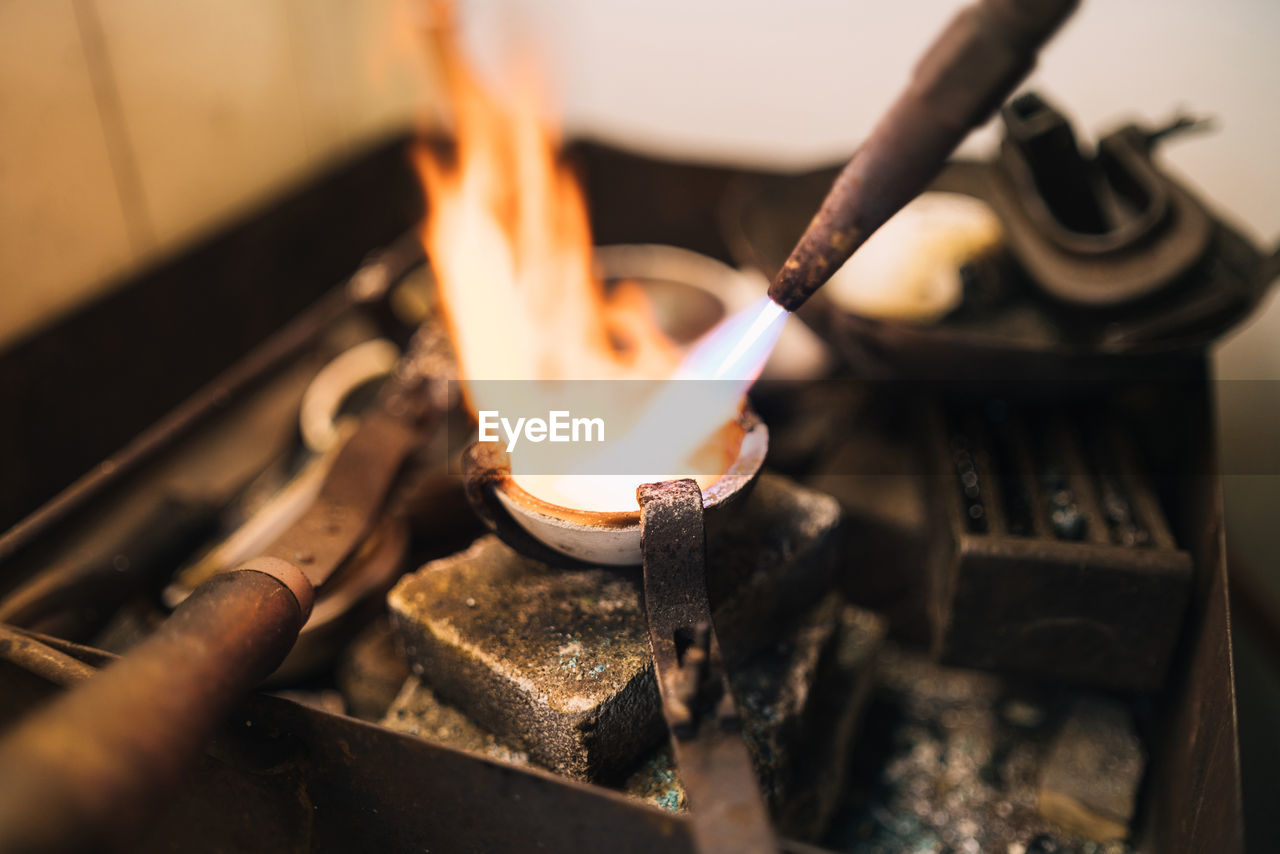 Closeup of burner with flame used for melting metal in small bowl during jewelry creation in professional workshop